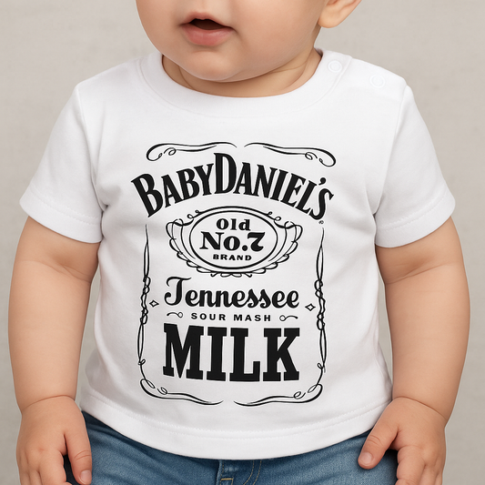 Baby draagt een wit T-shirt met een humoristische zwarte opdruk in de stijl van een whiskylabel, met de tekst “BabyDaniel’s Old No. 7 Brand Tennessee Sour Mash Milk”.